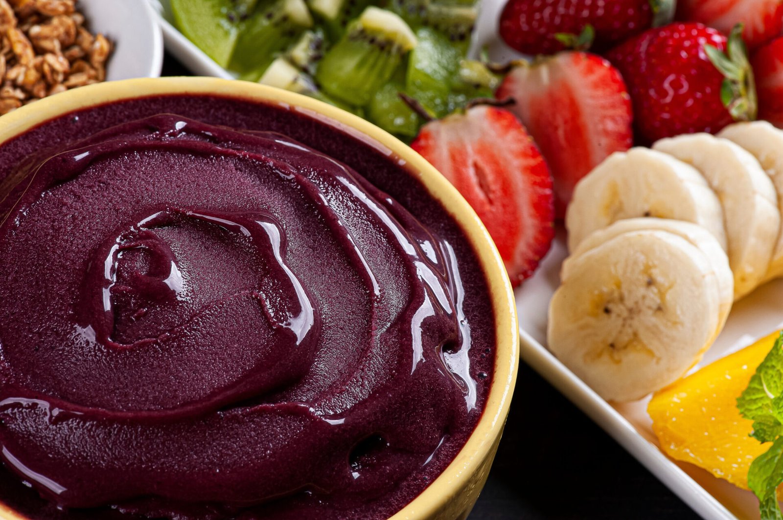 Imagem de uma tigela de açaí com frutas variadas ao lado.