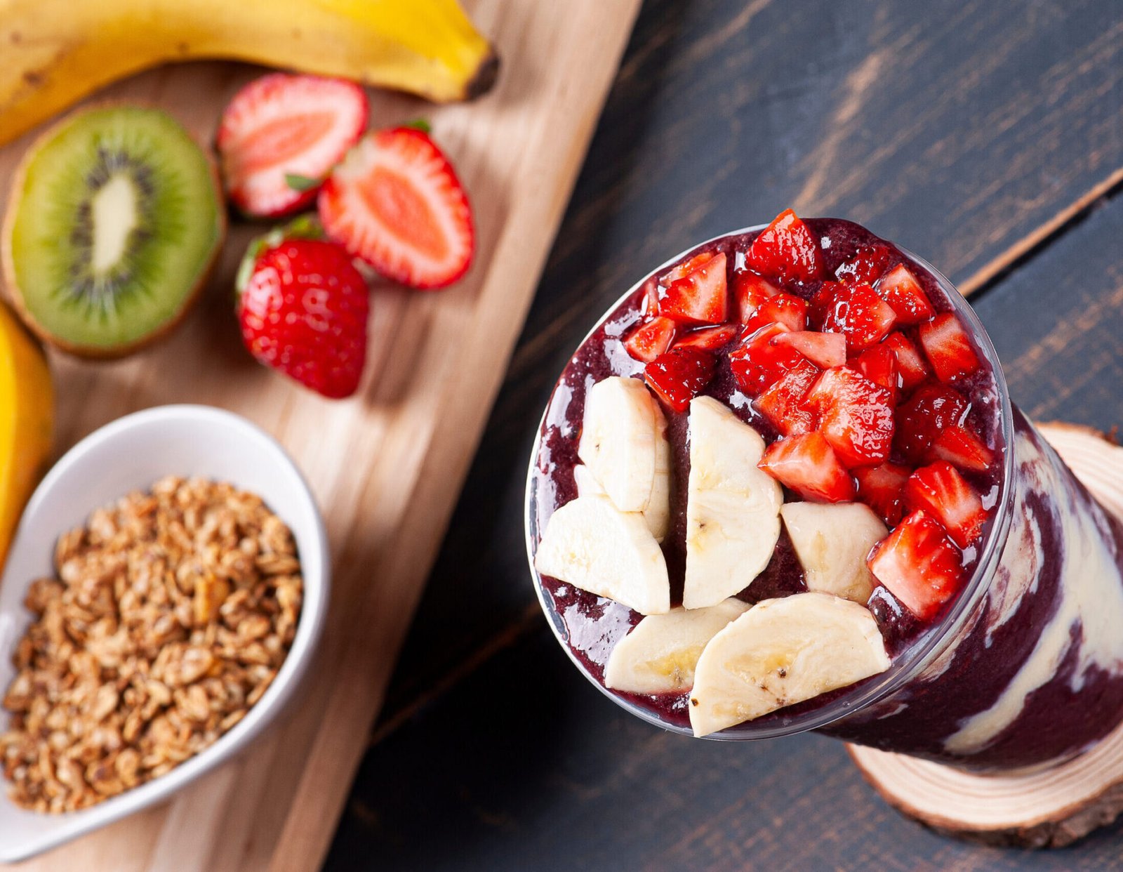 Imagem de um copo de açaí em cima de uma mesa com frutas variadas ao lado.